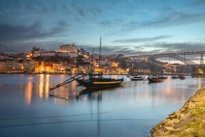 Captivating cityscape of Porto's riverside at dusk, featuring boats on the Douro River and illuminated landmarks.