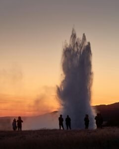 Captivating image of a geyser eruption with silhouetted spectators against a sunset sky in Iceland.