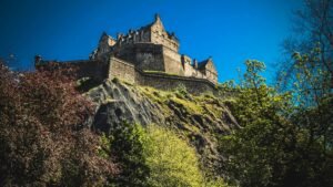 Iconic Edinburgh Castle atop Castle Rock under a clear blue sky, surrounded by lush greenery.
