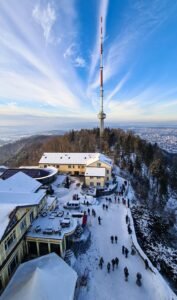 Snowy aerial view of Uetliberg Tower with surrounding buildings and trees in Zürich, Switzerland.